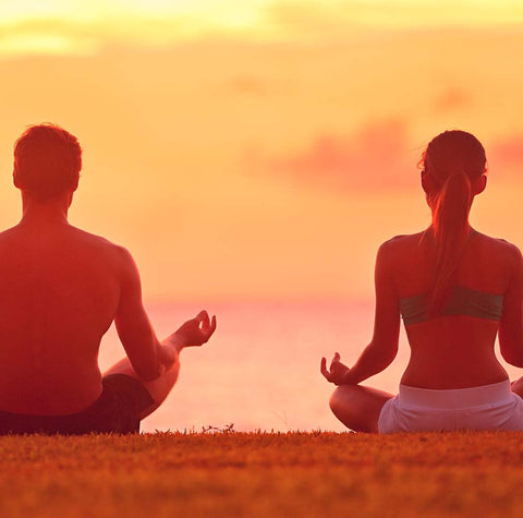 Man and woman meditating in front of the ocean in the sunset