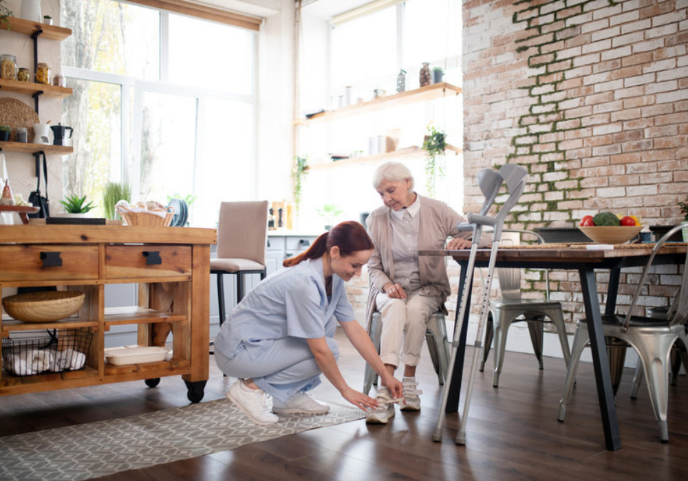 A female nurse wearing SAS nursing shoes helping an elderly woman velcro her shoes in an industrial kitchen