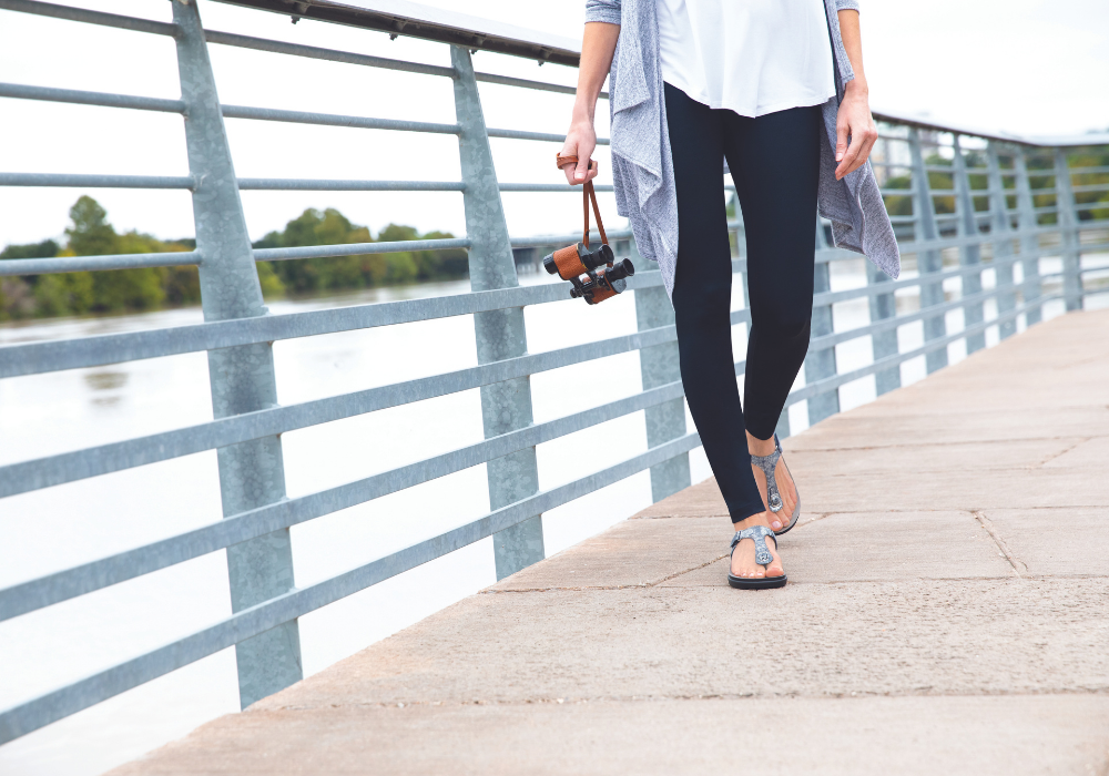 A woman wearing SAS walking sandals walking on a bridge above a lake