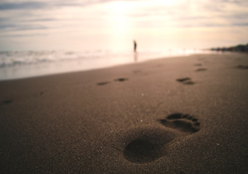 Footprints in the sand on a beach with a person in the water in the background