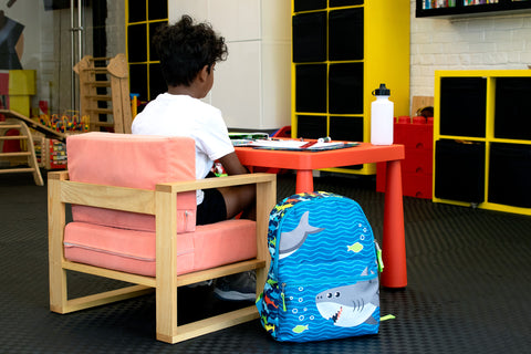 A young child sitting at a school desk with a printed backpack from Bags in Bulk