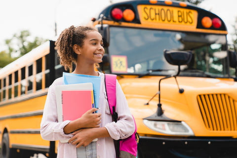 young student standing by a school bus