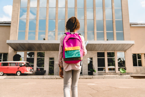 young girl wearing backpack walking into school