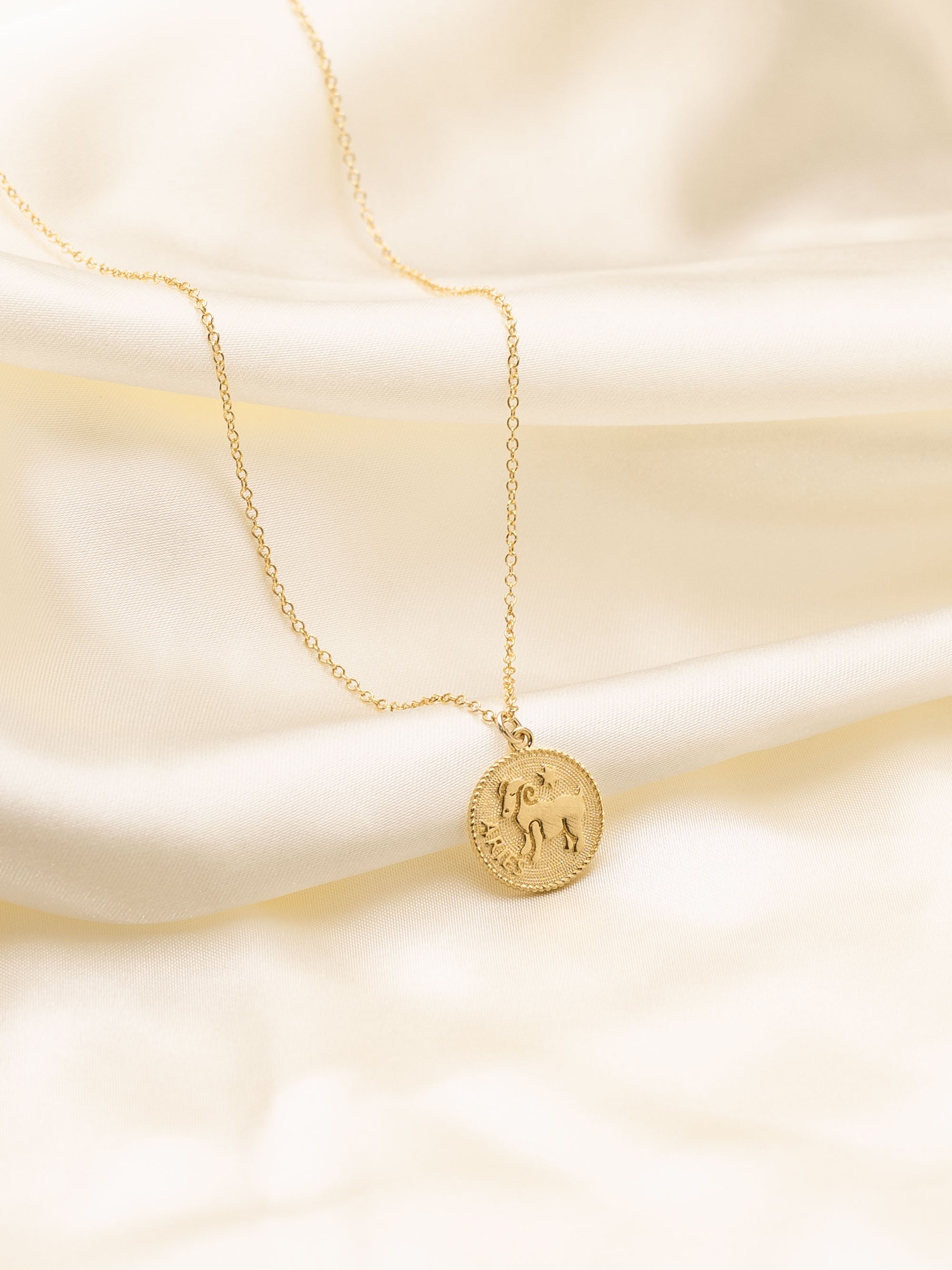 Elegant Aries zodiac necklace with a gold medallion featuring the ram symbol, showcased on a smooth white satin fabric.