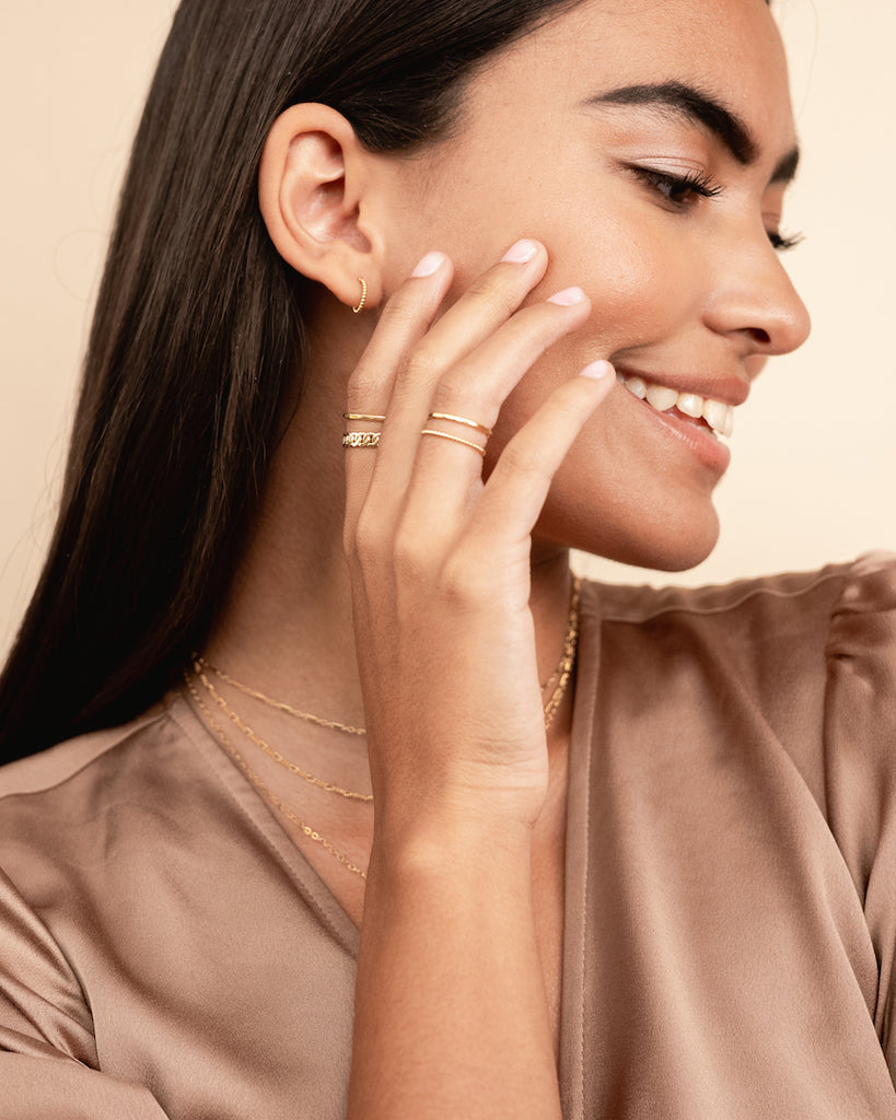 Model smiling while wearing the dainty, nickel-free Beaded Hoop Studs from Katie Dean Jewelry, paired with a selection of delicate gold rings.