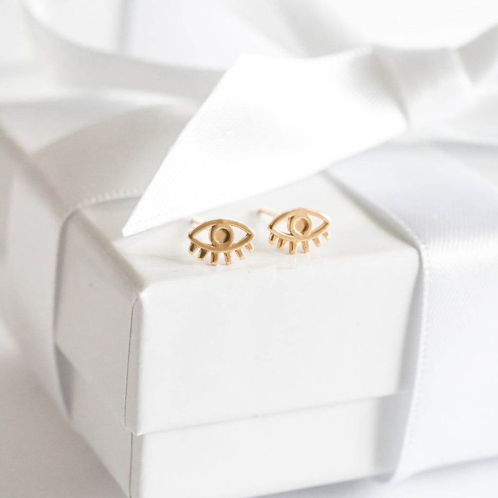 Dainty gold Evil Eye Stud Earrings as seen on a gift box, made in America by Katie Dean Jewelry