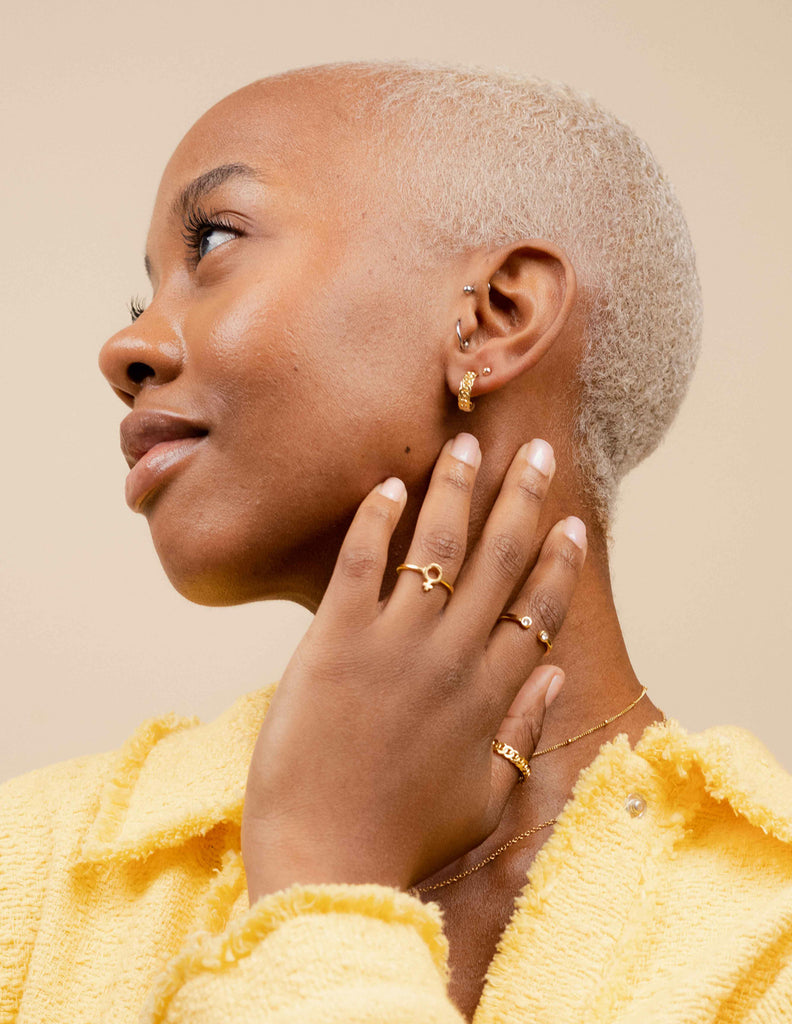 An elegant woman in a yellow textured top showcases Katie Dean Jewelry, featuring the Female Symbol Ring on her index finger, complementing her graceful style with its delicate design.
