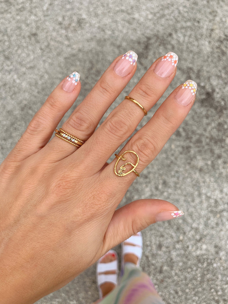 Artistic hand pose showcasing Katie Dean Jewelry rings including the Artist Face Ring with floral nail design.