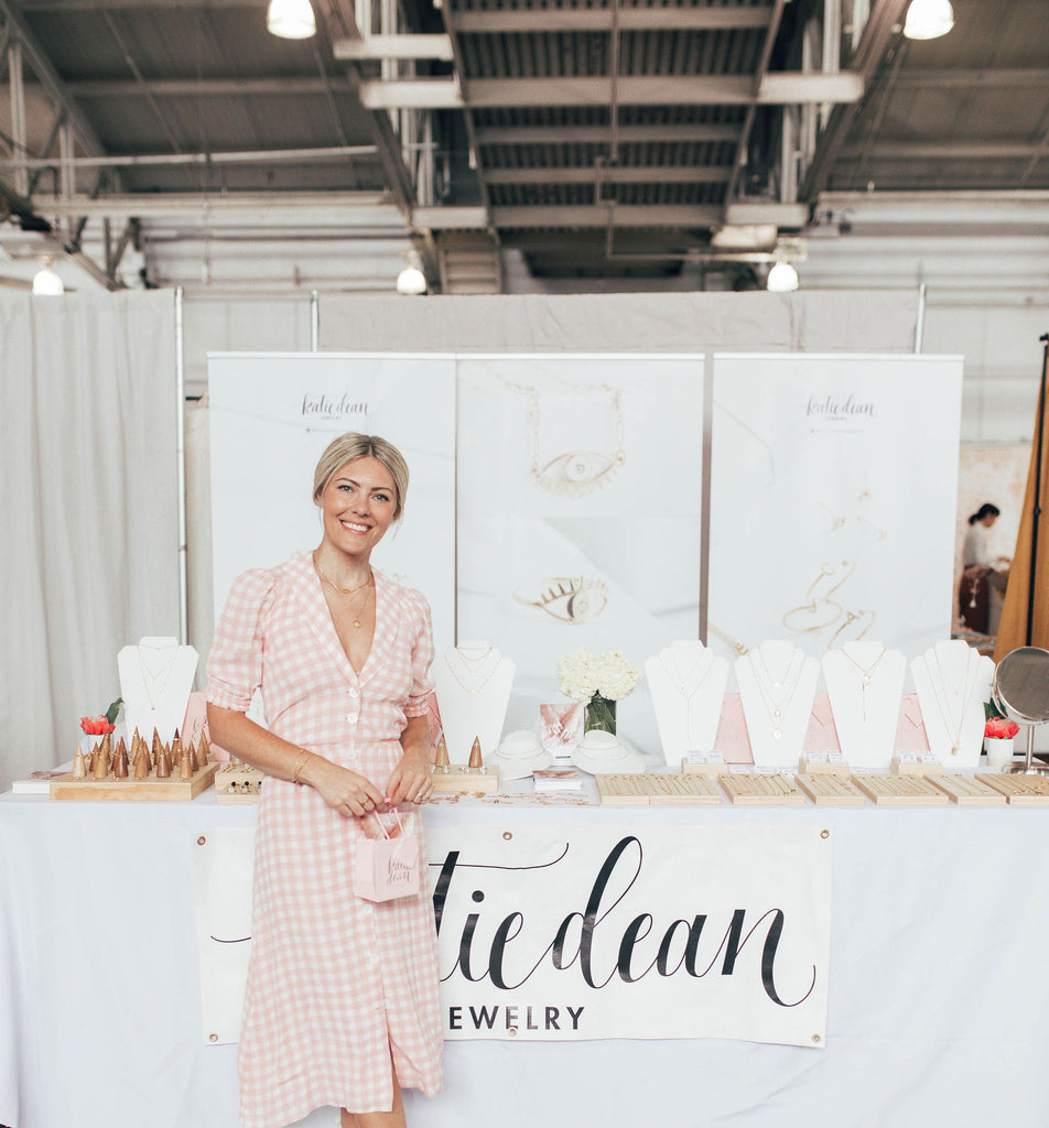 Photo of Katie Dean at a Renegade Craft Fair in San Francisco, in front of her booth with her made in America dainty jewelry.