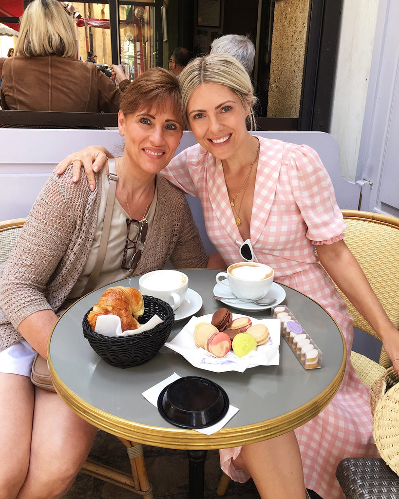 Picture showing jewelry designer, Katie Dean with her Mom at a bistro table in Aix en Provence, France posing for a photo with their cafe snacks and coffee.