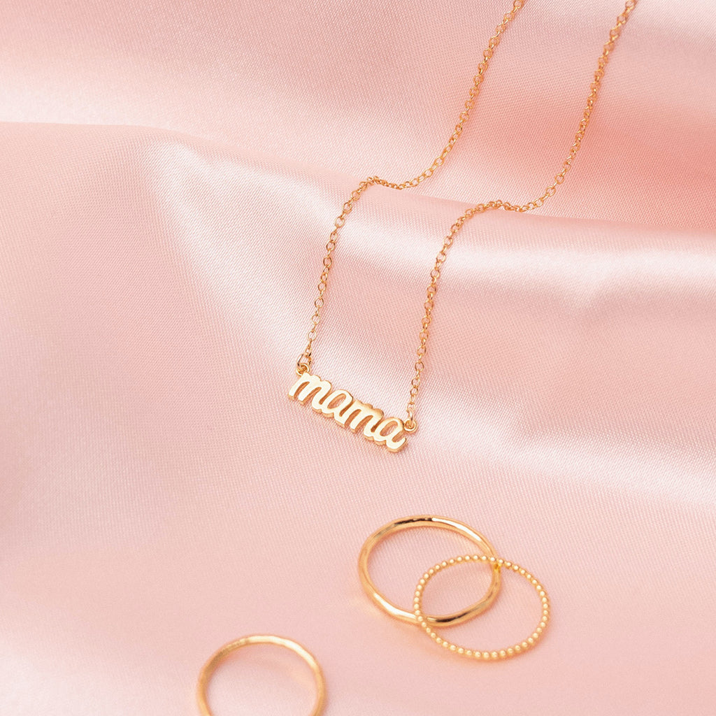 The dainty gold Mama Necklace draped gracefully on a pink satin sheet, made in America by Katie Dean Jewelry, perfect for the minimalist.