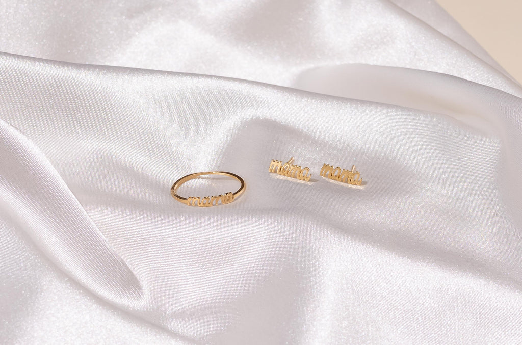 Dainty gold stacking Mama Ring alongside the Mama Studs on a white piece of satin.