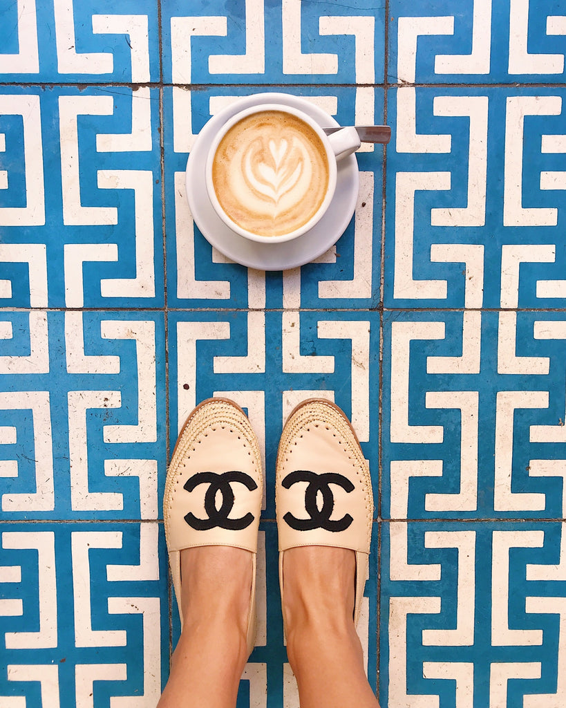 Katie Dean takes a chic coffee break in Paris with designer Chanel espadrilles and a cappuccino on a mosaic tile floor.