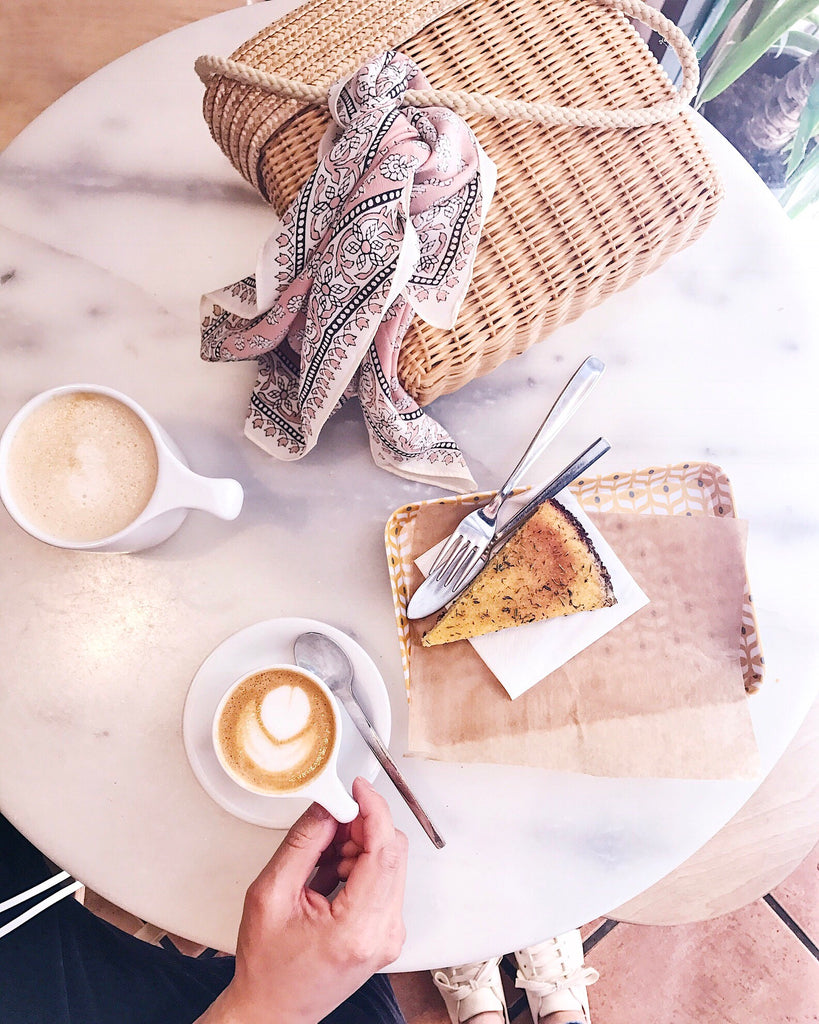 Onna Coffee, Barcelona Spain white marble table with cappucino and polenta cake on plates and wicker purse.