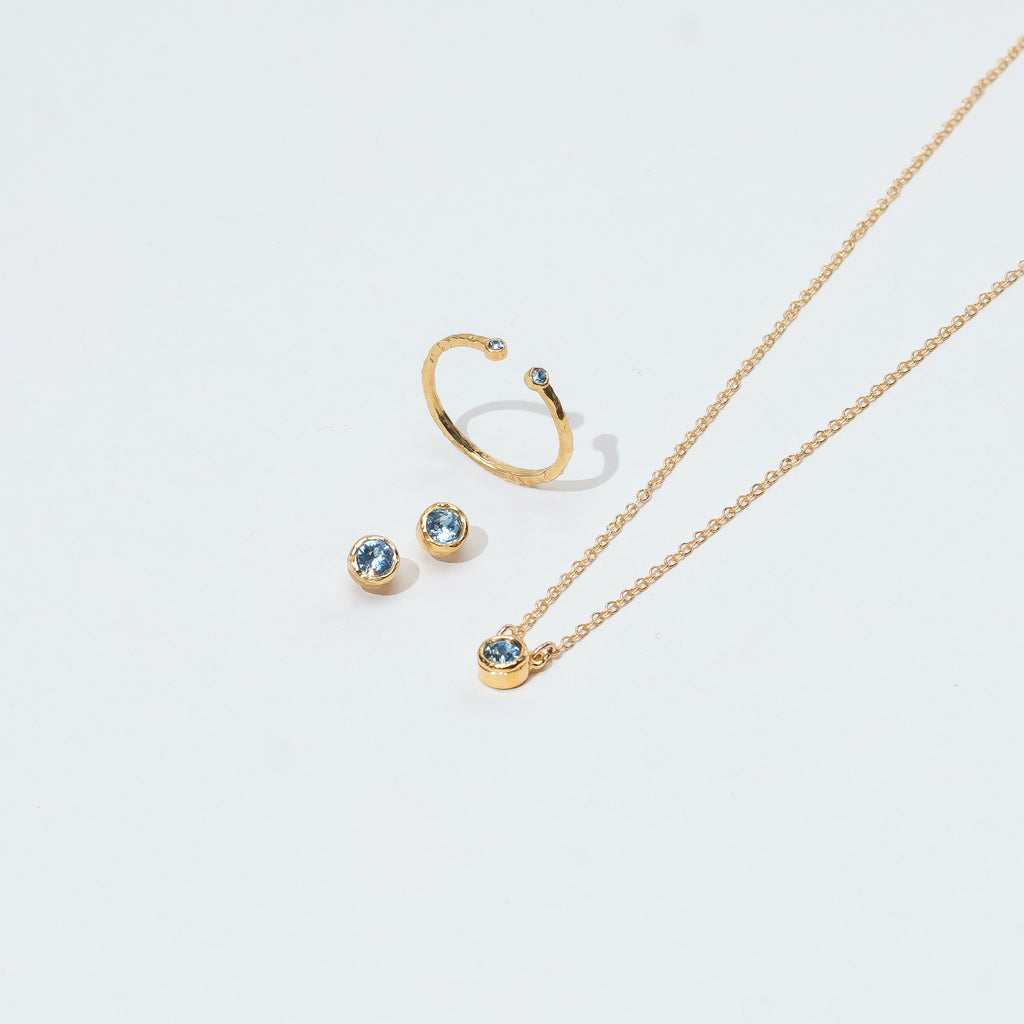 Elegant March birthstone jewelry set made in America by Katie Dean Jewelry with aquamarine crystals set in gold, including a necklace, ring, and stud earrings.