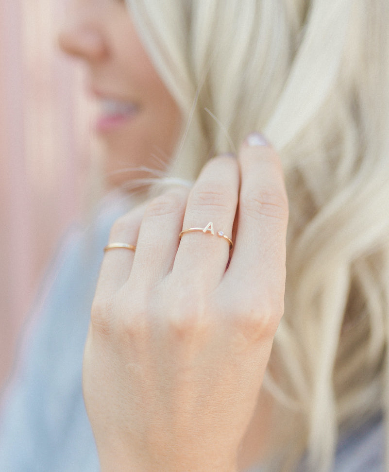 Close-up of a hand wearing a delicate gold 'A' initial ring by Katie Dean Jewelry.