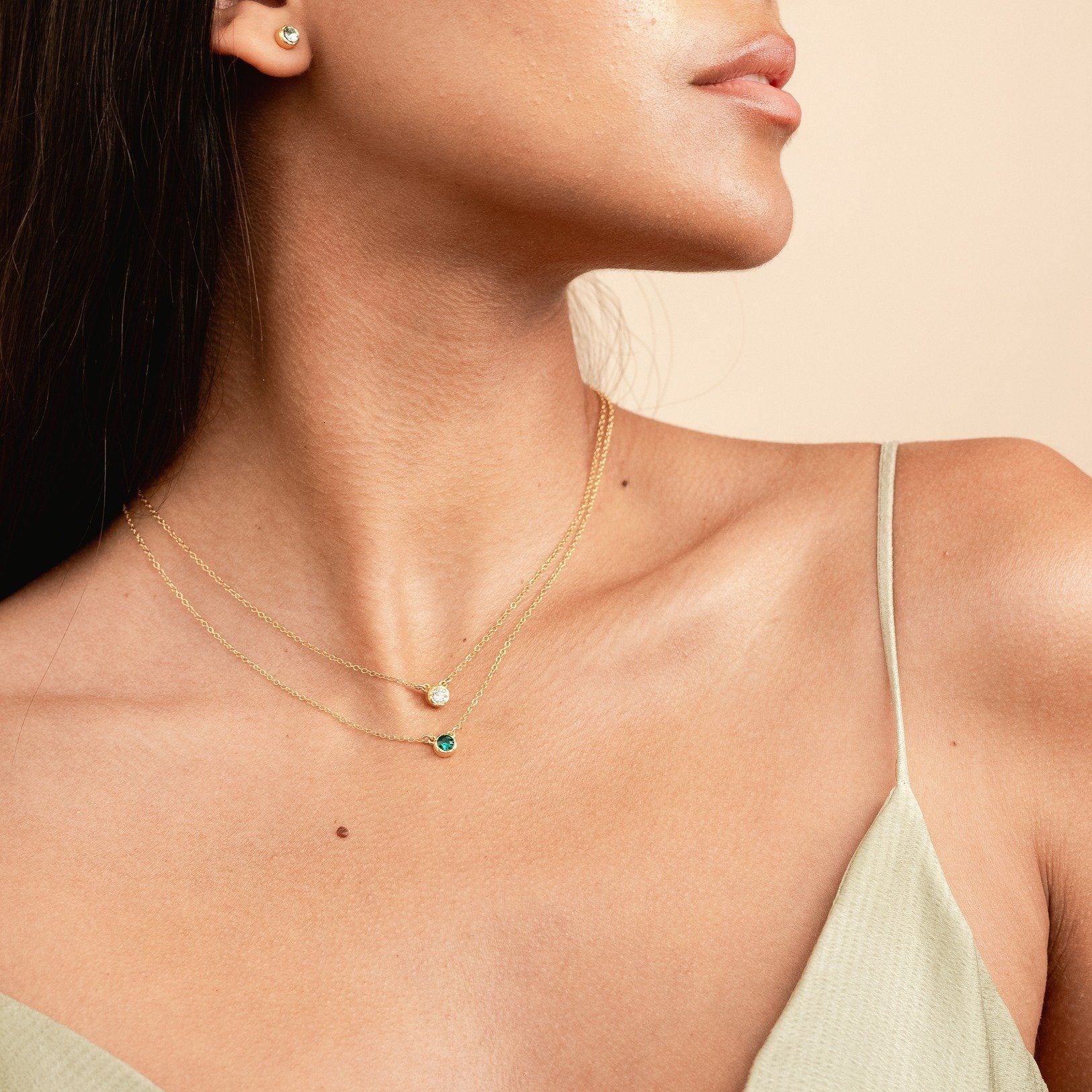 Model wearing the dainty gold birthstone necklaces in April (crystal) and May (emerald) and the August stud earrings made by Katie Dean Jewelry