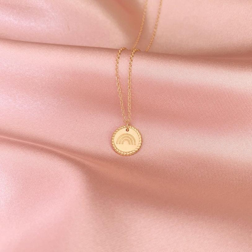 The dainty gold Rainbow Necklace as seen draped on a pink piece of satin, handmade in America by Katie Dean Jewelry. A symbol for hope.