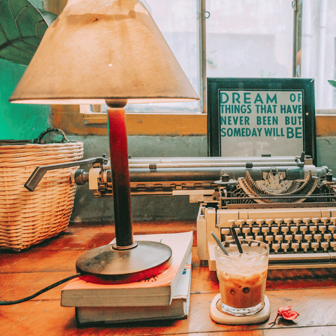 Lamp on desk with typewriter books and an iced coffee