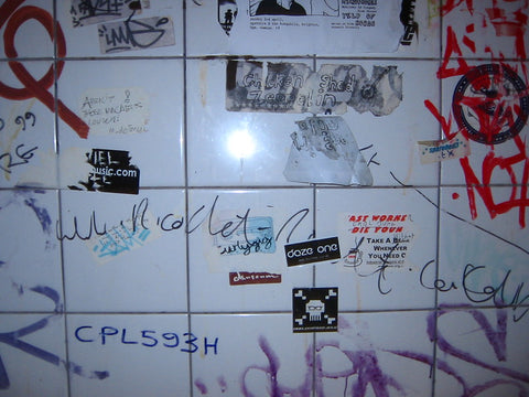 Bathroom wall with stickers and graffiti.