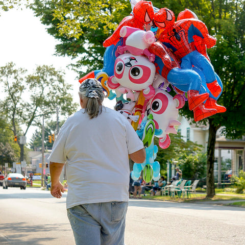 Woman walking down a street in a parade holding character balloons.