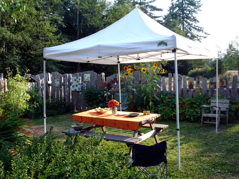 White canopy tent in lush garden with picnic table underneath.