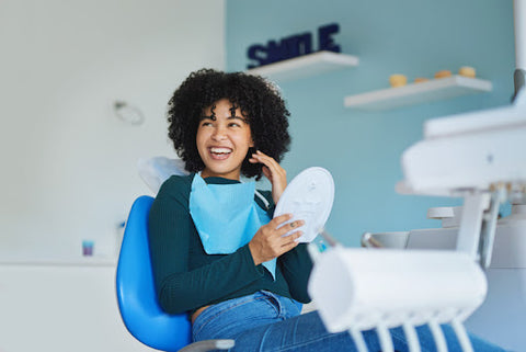 woman in dentist chair smiling and holding mirror