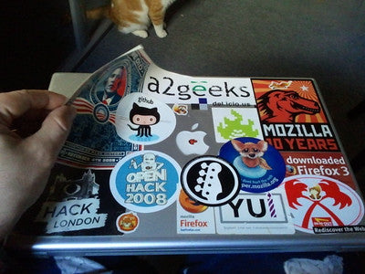 A hand removing sticker skin with stickers on a laptop.