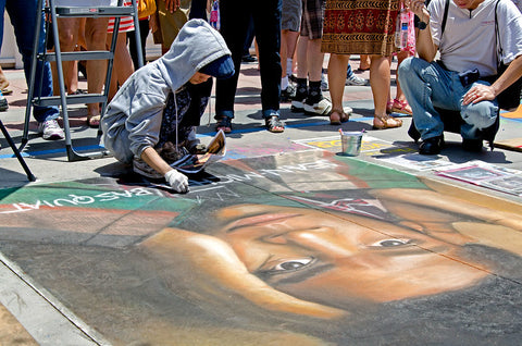 Street artist using chalk to draw on pavement.