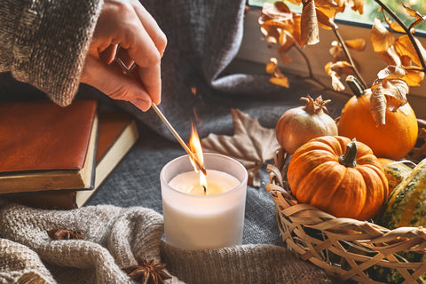 Hand lighting a fall-scented candle with a fall backdrop