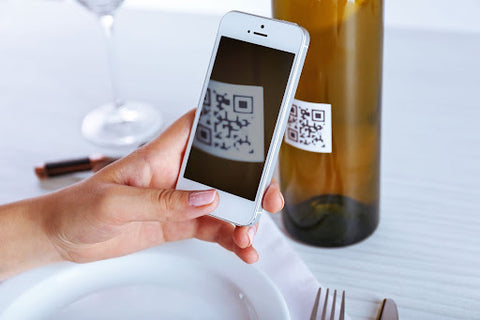 Hand with a phone scanning a QR code on a bottle on a table.