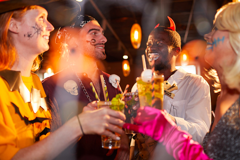 Happy group of people dressed in Halloween costumes drinking festive drinks