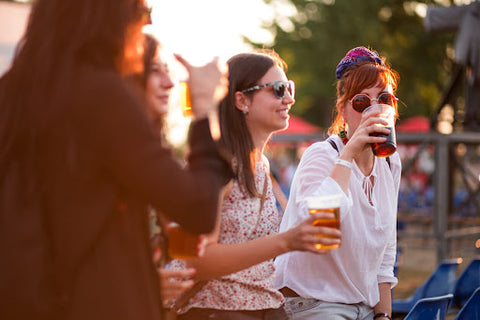 Smiling women drinking glasses of beer outside at sunset.
