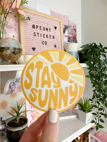 Stay Sunny orange sticker held in front of cute desk setup.