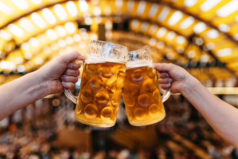 Two hands clinking full pints of beer together at a beer festival.
