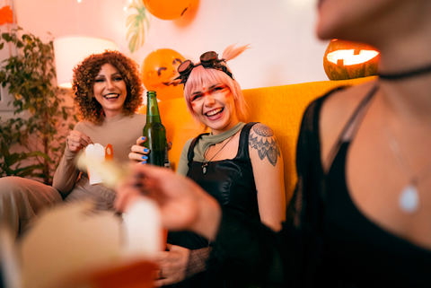 Two women smiling at a Halloween party, one drinking a beer