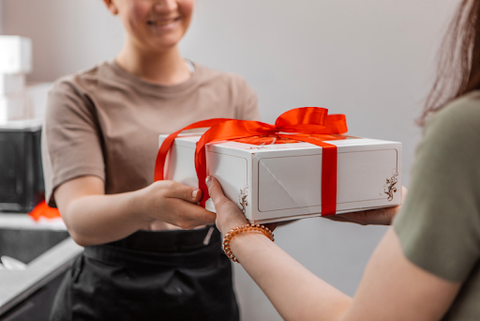 Woman handing wrapped gift with red ribbon to another person