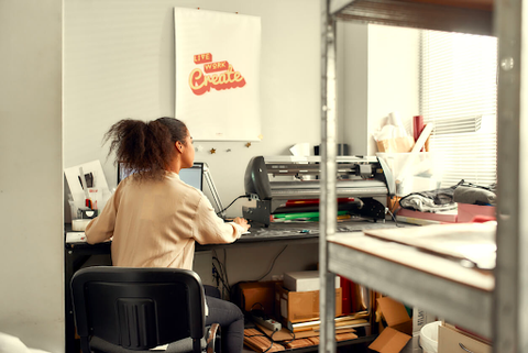 Woman printing art in an office space with sign "live work create."