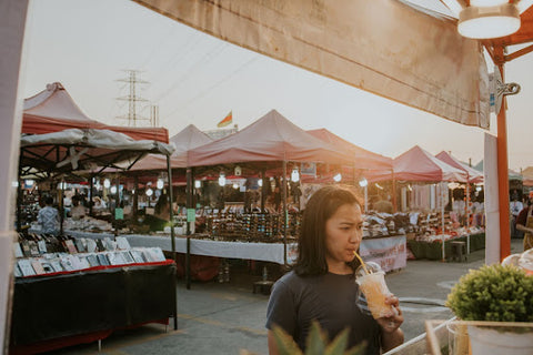 Woman sipping an iced drink at a craft fair at sunset.