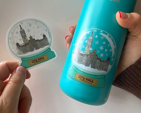 Snow globe sticker and blue water bottle with snow globe sticker held up.