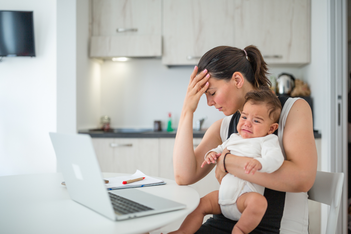 woman holding fussy baby with laptop nearby-5 places to find breastfeeding support- Mila's Keeper