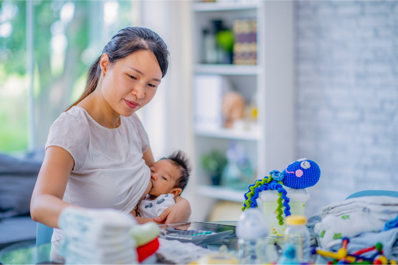 mother nurses baby while multi-tasking-how much water should you drink while breastfeeding- Mila's Keeper