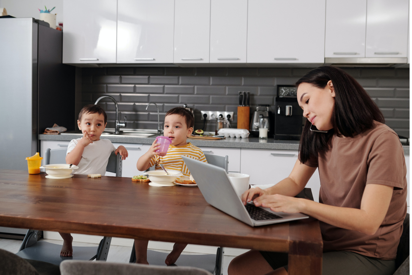 mother works on laptop with children at table- US maternity leave compared to other countries- Mila's Keeper