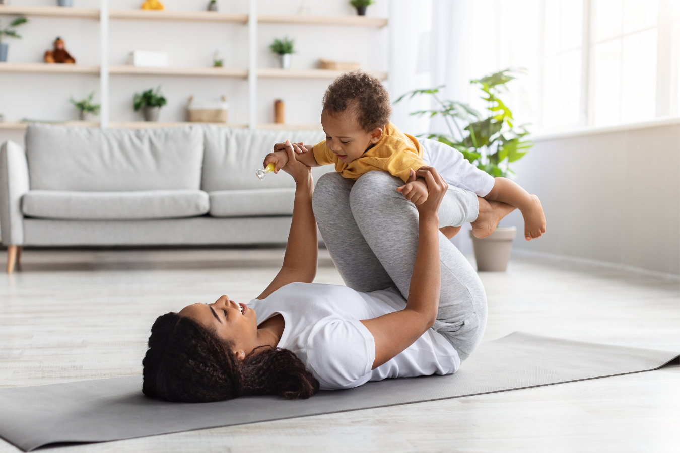 mom lays on floor while doing airplane with baby-Origins of Breastfeeding in African Culture- Mila's Keeper