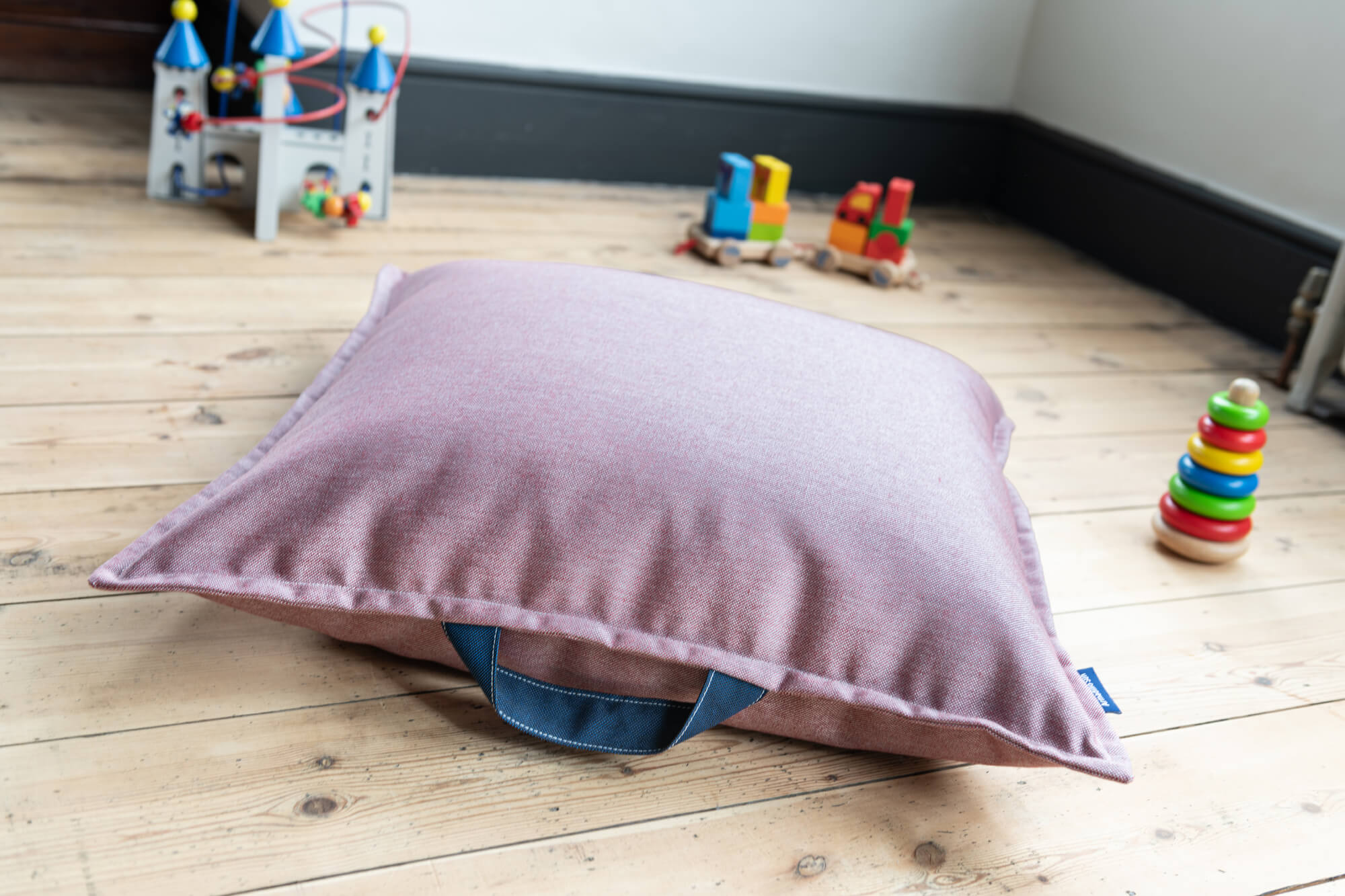 Kids floor cushion in pinky red surrounded by toys