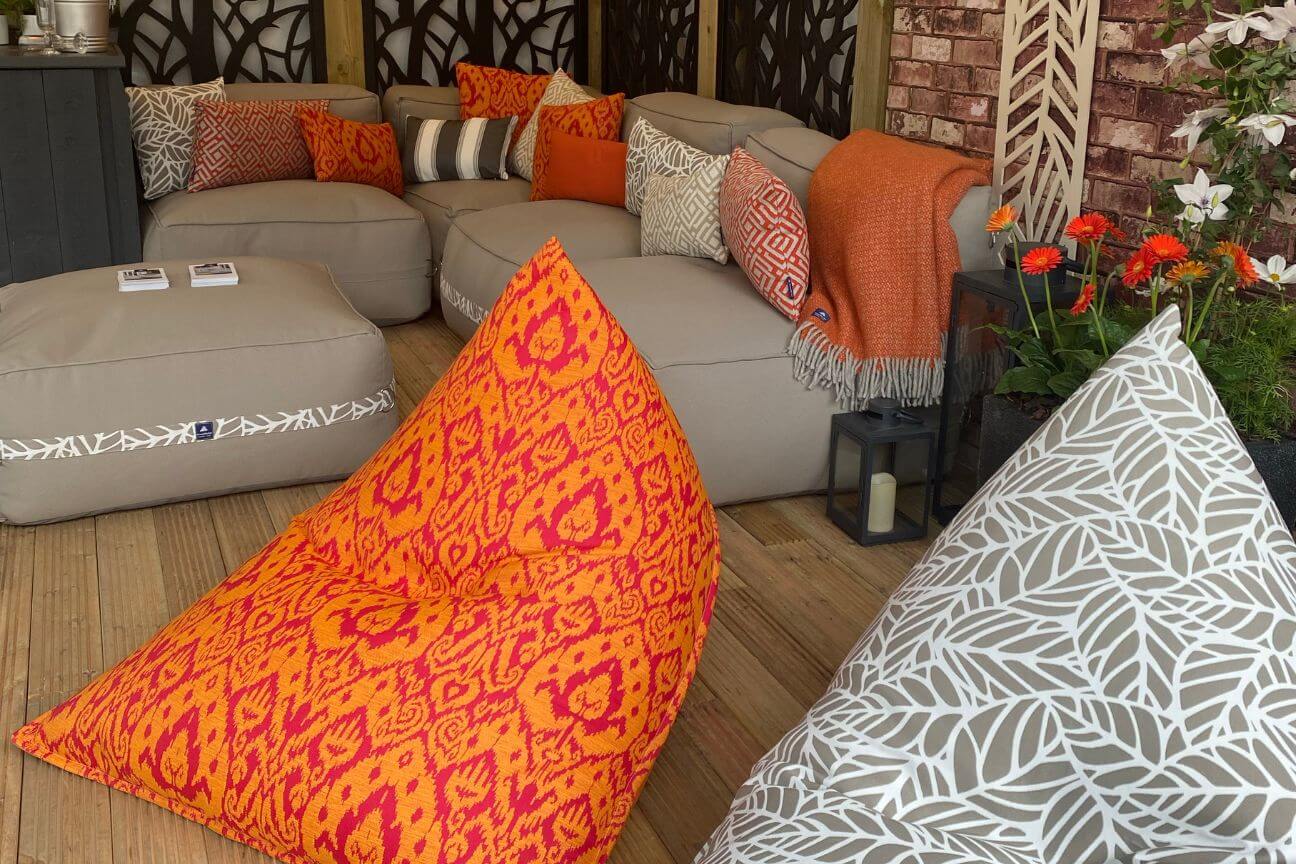 A bold orange and pink garden bean bag under a pergola with a garden sofa accessorised with orange and grey garden cushions