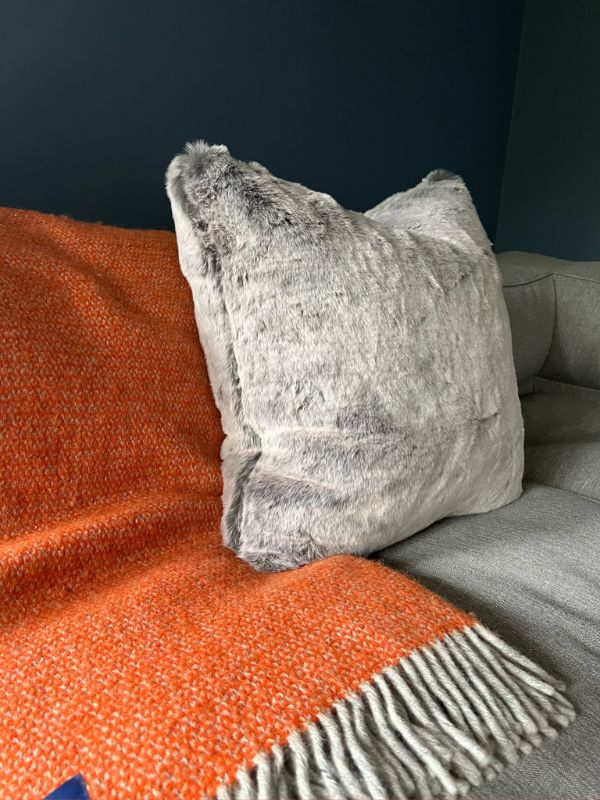 Silvery grey faux fur cushion against a pumpkin orange handwoven throw on an easy access sofa