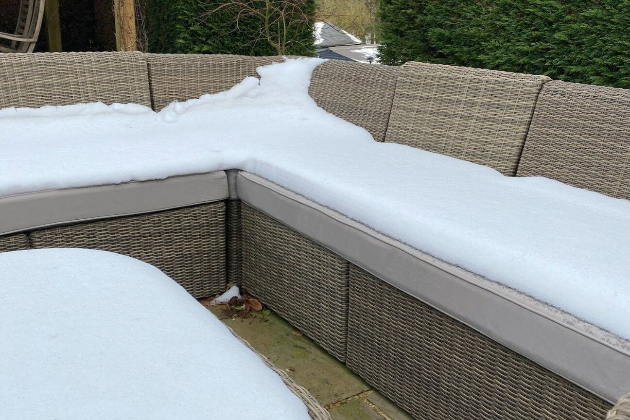 A rattan garden sofa with customised garden furniture cushions outdoors in winter and covered in a thick layer of snow