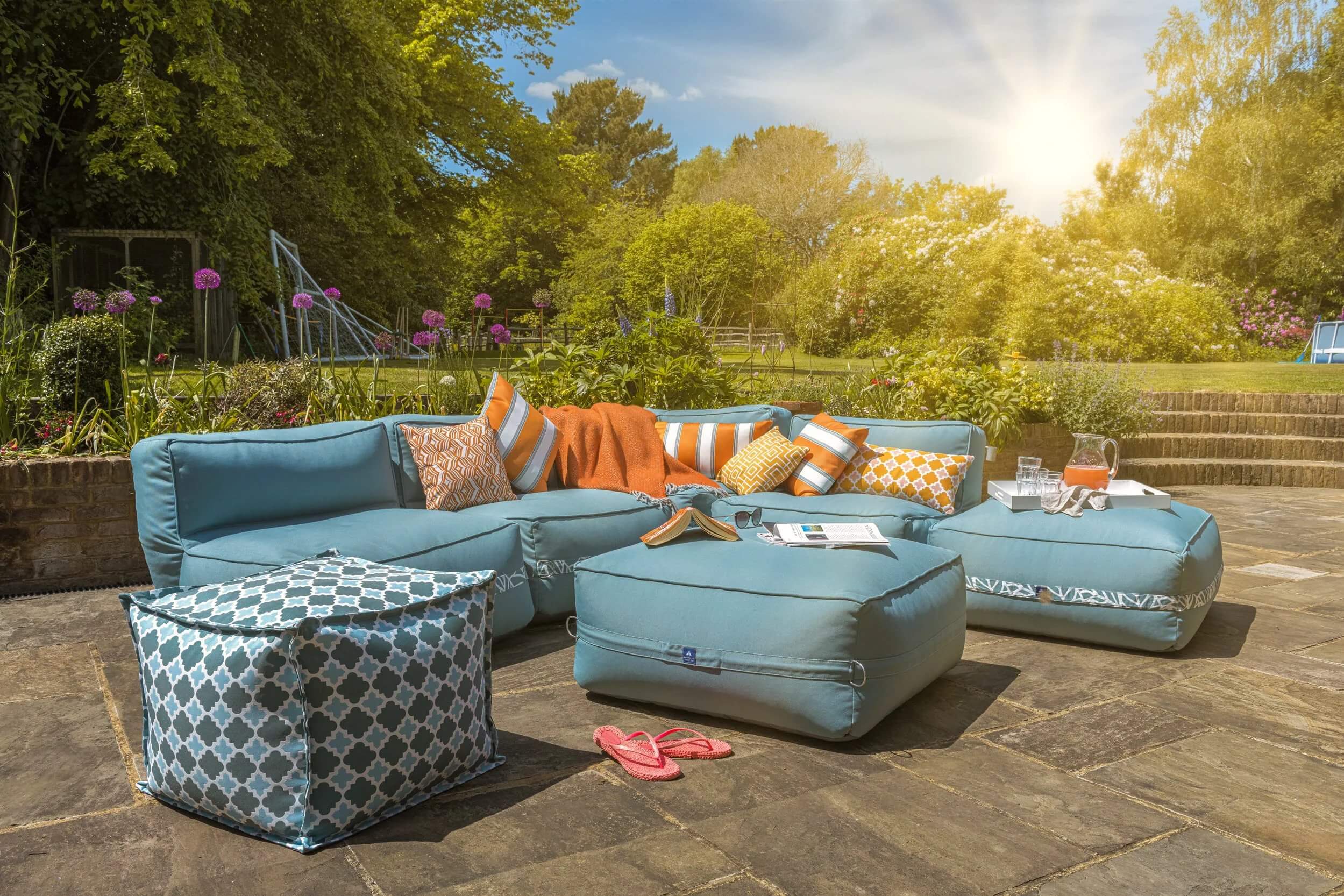 A garden sofa decorated with bright orange cushions is set-up for outdoor entertaining on a sunny patio