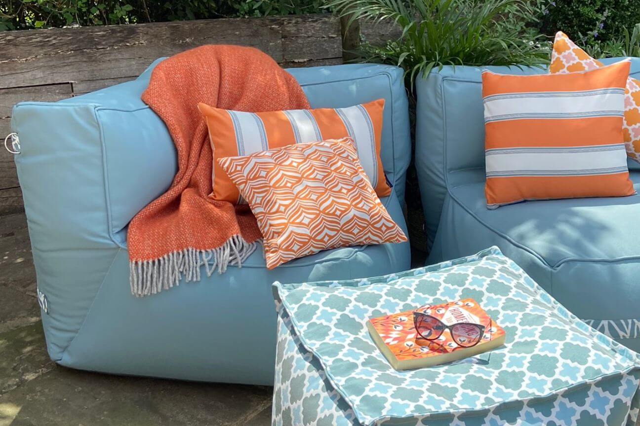 A soft fabric garden sofa corner chair is accessorised with orange and white patterned cushions and a lambswool throw.